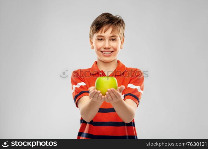 food, healthy eating and people concept - portrait of happy smiling boy in red polo t-shirt holding green apple over grey background. portrait of happy smiling boy holding green apple