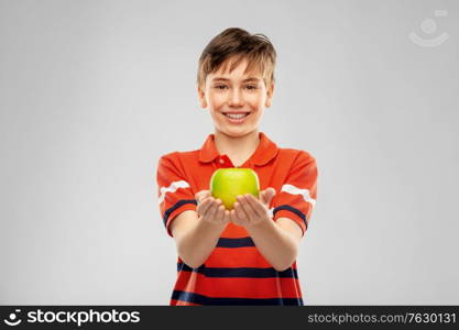 food, healthy eating and people concept - portrait of happy smiling boy in red polo t-shirt holding green apple over grey background. portrait of happy smiling boy holding green apple