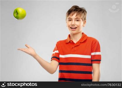 food, healthy eating and people concept - portrait of happy smiling boy in red polo t-shirt throwing green apple over grey background. portrait of happy smiling boy throwing green apple