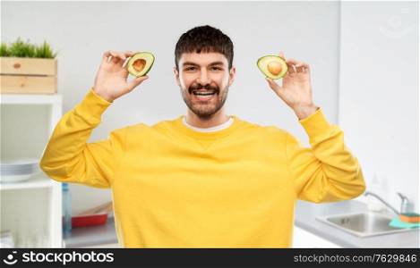 food, healthy eating and people concept - smiling young man in yellow sweatshirt with avocado over home kitchen background. happy young man in yellow sweatshirt with avocado