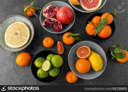 food, healthy eating and vegetarian concept - close up of citrus fruits in bowls on stone table. close up of citrus in bowls fruits on stone table