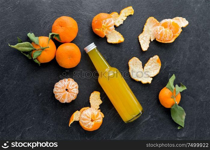 food , healthy eating and vegetarian concept - glass bottle of fruit juice and peeled mandarins on slate table top. glass bottle of fruit juice and peeled mandarins