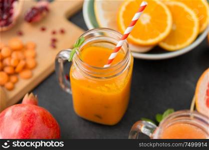 food , healthy eating and vegetarian concept - mason jar glass of orange or carrot juice with paper straw and citrus fruits on slate table top. mason jar glass of carrot juice with paper straw