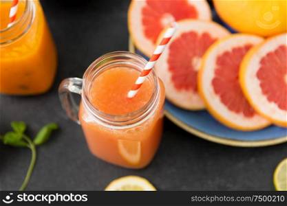 food , healthy eating and vegetarian concept - mason jar glass of grapefruit juice with paper straw and citrus fruits on slate table top. mason jar glass of fruit juice with paper straw
