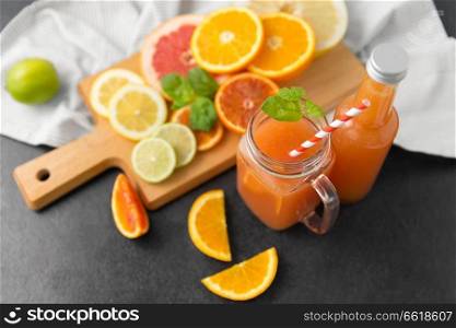 food , healthy eating and vegetarian concept - mason jar glass with juice and citrus fruits on slate table top. mason jar glass with juice and fruits on table