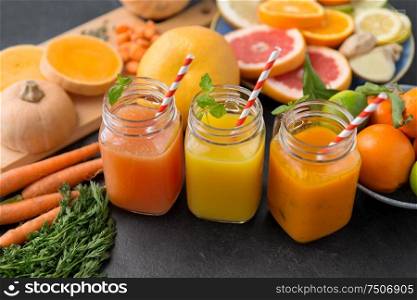 food , healthy eating and vegetarian concept - mason jar glasses of orange and carrot juices with paper straws, fruits and vegetables on slate table. mason jar glasses of vegetable juices on table