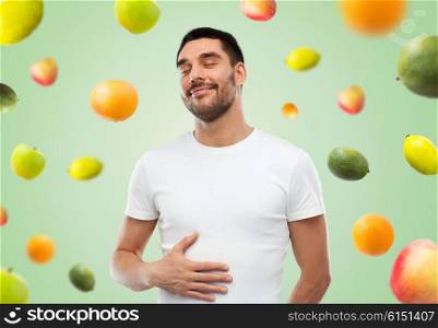 food, healthy eating, diet and people concept - happy full man touching his tummy over green background with falling fruits