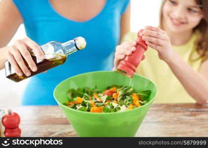 food, healthy eating, family and people concept - close up of happy girl and mother cooking salad for dinner and adding spices in kitchen