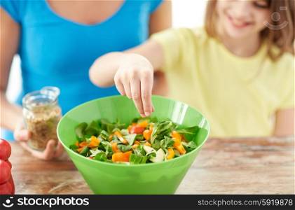 food, healthy eating, family and people concept - close up of happy girl and mother cooking salad for dinner and adding spices in kitchen