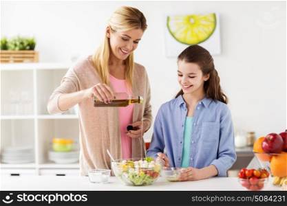 food, healthy eating, family and people concept - happy mother and daughter cooking and adding olive oil to vegetable salad for dinner at home kitchen. happy family cooking salad at home kitchen. happy family cooking salad at home kitchen