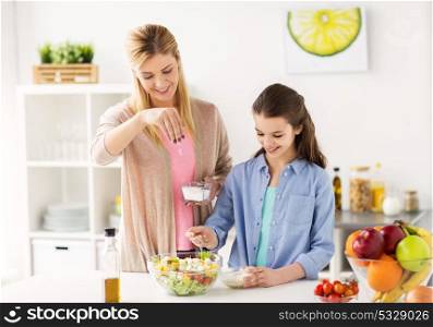 food, healthy eating, family and people concept - happy mother and daughter cooking and salting vegetable salad for dinner at home kitchen. happy family cooking salad at home kitchen