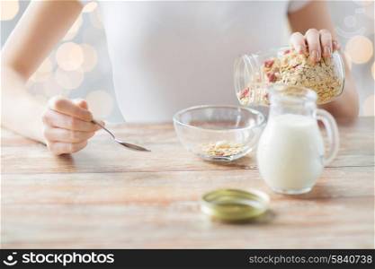 food, healthy eating, people and diet concept - close up of woman eating muesli with milk for breakfast over holidays lights background