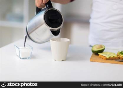 food, healthy eating, people and diet concept - man with kettle making tea and having avocado sandwiches for breakfast at home kitchen. man with kettle making tea for breakfast at home