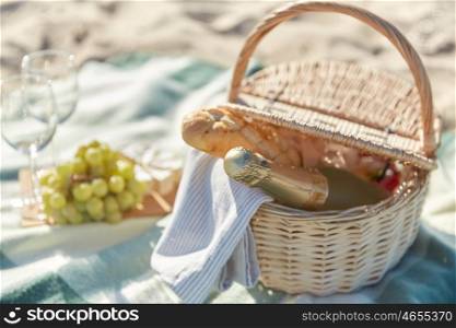 food, holidays and celebration concept - close up of picnic basket champagne bottle and french roll bread on summer beach