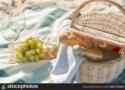 food, holidays and celebration concept - close up of picnic basket with grapes, wine glasses, cheese and champagne bottle on summer beach