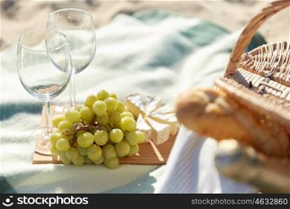 food, holidays, celebration and summer concept - close up of picnic basket with grapes, wine glasses and cheese on beach