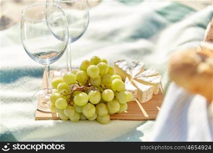 food, holidays, celebration and summer concept - close up of picnic with grapes, wine glasses and cheese on beach