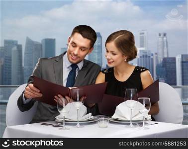 food, holidays, lunch, dinner and people concept - smiling couple with menus at restaurant over city background