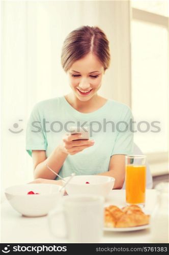 food, home and technology concept - smiling young woman with smartphone reading news and having breakfast at home