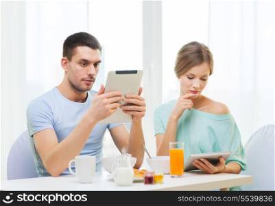 food, home, couple and technology concept - concentrated couple with tablet pc reading news and having breakfast at home