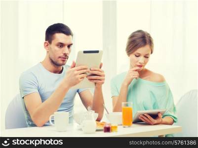 food, home, couple and technology concept - concentrated couple with tablet pc reading news and having breakfast at home