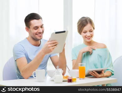 food, home, couple and technology concept - smiling couple with tablet pc reading news and having breakfast at home