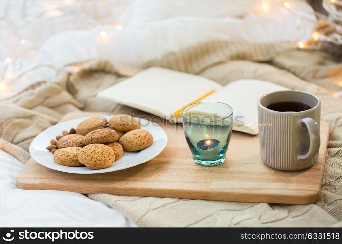 food, hygge and comfort concept - oatmeal cookies, tea, diary and candle in holder at home. cookies, tea and candle in holder at home