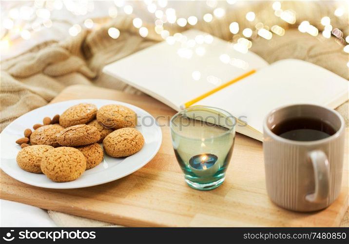 food, hygge and comfort concept - oatmeal cookies, tea, diary and candle in holder at home. cookies, tea and candle in holder at home