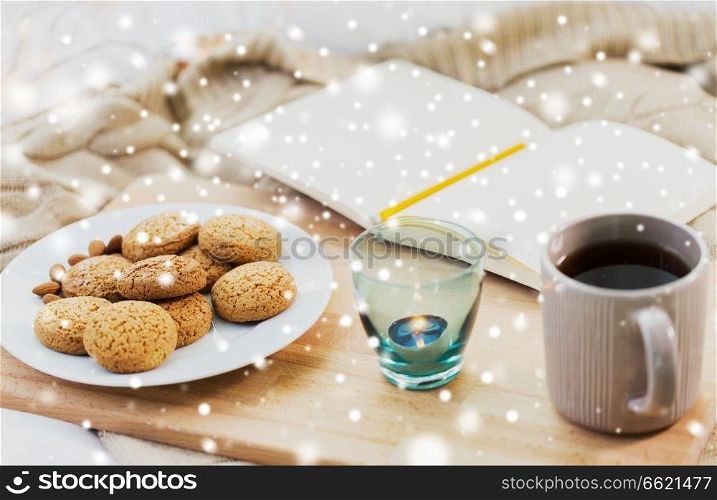 food, hygge and winter concept - oatmeal cookies, tea, diary and candle in holder at home over snow. cookies, tea and candle at home over snow