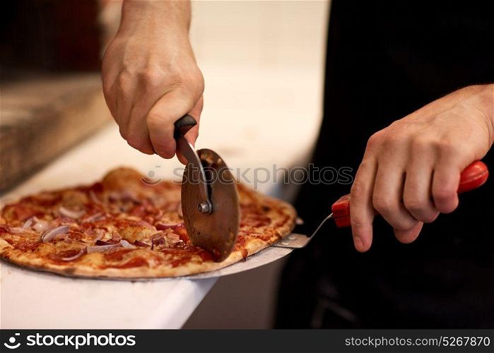 food, italian kitchen and cooking concept - cook hands with cutter cutting pizza to pieces at pizzeria. cook hands cutting pizza to pieces at pizzeria