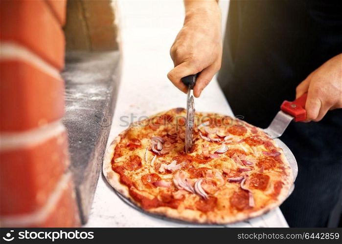 food, italian kitchen and cooking concept - cook hands with cutter cutting pizza to pieces at pizzeria. cook hands cutting pizza to pieces at pizzeria