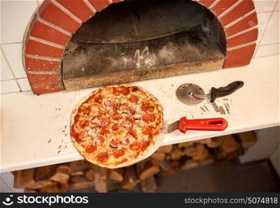 food, italian kitchen, culinary and cooking concept - baked pizza on peel and cutter at pizzeria oven . baked pizza on peel and cutter at pizzeria oven