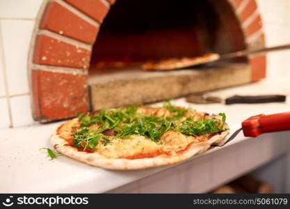 food, italian kitchen, culinary and cooking concept - baked pizza with arugula on peel at pizzeria oven . baked pizza on peel at pizzeria oven