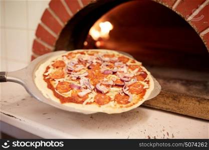 food, italian kitchen, culinary, baking and cooking concept - peel placing pizza into oven at pizzeria. peel placing pizza into oven at pizzeria