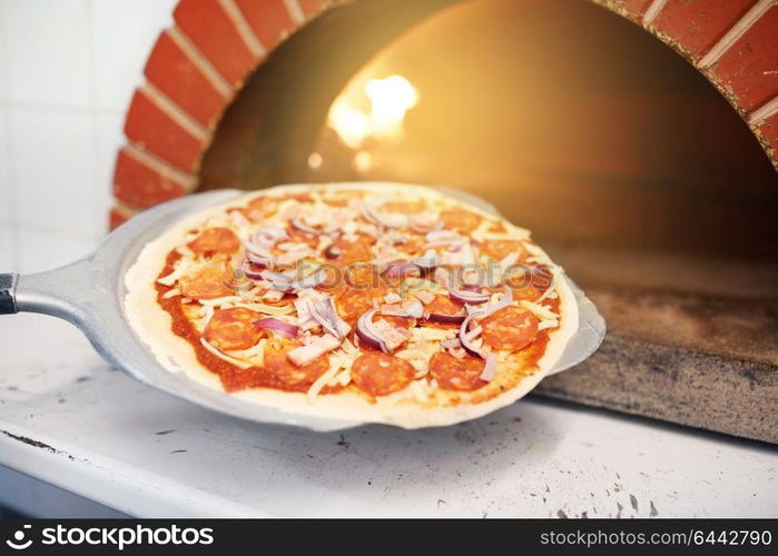 food, italian kitchen, culinary, baking and cooking concept - peel placing pizza into oven at pizzeria. peel placing pizza into oven at pizzeria