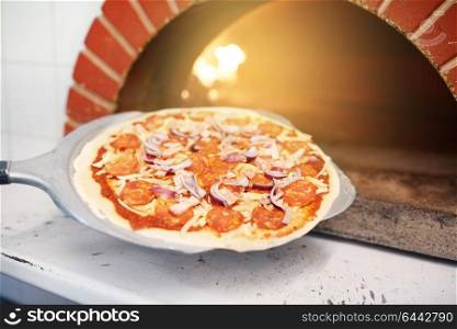 food, italian kitchen, culinary, baking and cooking concept - peel placing pizza into oven at pizzeria. peel placing pizza into oven at pizzeria