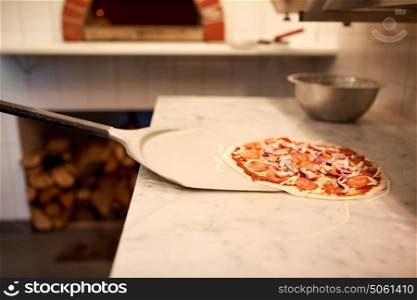 food, italian kitchen, culinary, baking and cooking concept - peel taking pizza off table at pizzeria. peel taking pizza off table at pizzeria