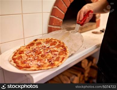 food, italian kitchen, culinary, people and cooking concept - chef placing pizza from peel to plate at pizzeria. chef placing pizza from peel to plate at pizzeria
