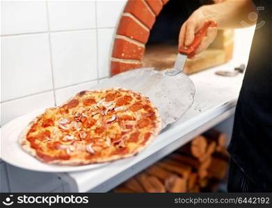 food, italian kitchen, culinary, people and cooking concept - chef placing pizza from peel to plate at pizzeria. chef placing pizza from peel to plate at pizzeria