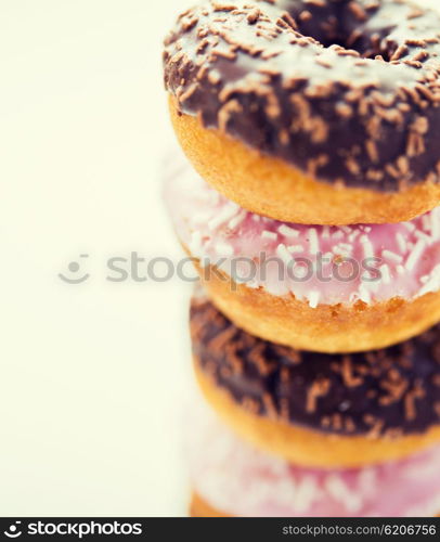 food, junk-food and eating concept - close up of glazed donuts pile over white