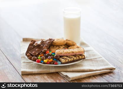 food, junk-food and unhealthy eating concept - close up of chocolate, oatmeal cookies, drop candies with muesli bars on plate and glass of milk. chocolate, cookies, candies and muesli bars
