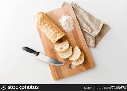 food, junk-food and unhealthy eating concept - close up of white ciabatta bread on wooden cutting board, knife and kitchen towel. close up of white ciabatta bread on cutting board