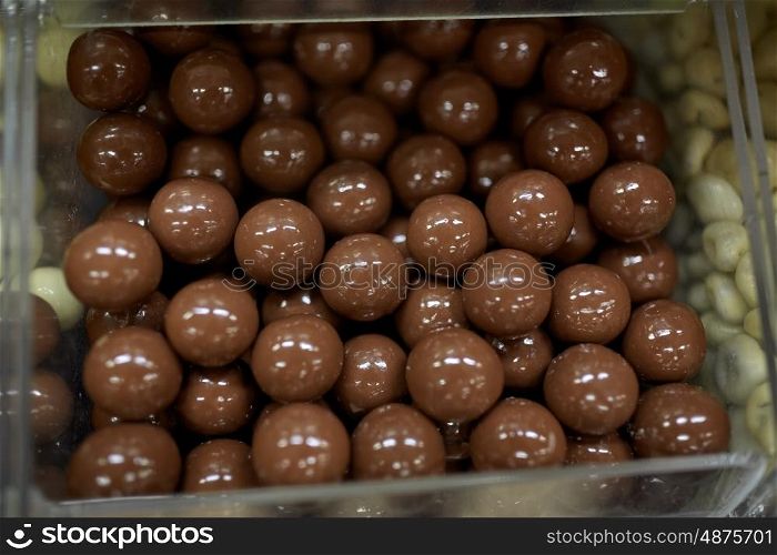 food, junk-food, confectionery and unhealthy eating concept - close up of chocolate dragee balls in transparent plastic box at candy shop