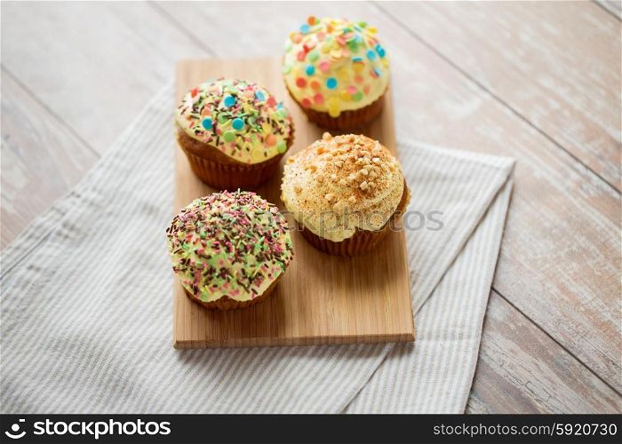 food, junk-food, culinary, baking and eating concept - close up of glazed cupcakes or muffins on wooden board
