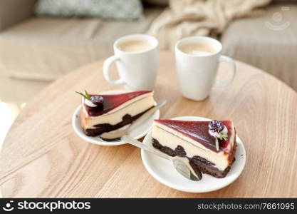 food, junk-food, culinary, baking and holidays concept - pieces of delicious cake on saucers with spoons and coffee cups on wooden table. pieces of chocolate cake on wooden table