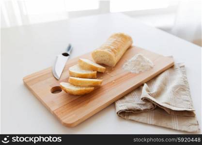 food, junk-food, diet and unhealthy eating concept - close up of white bread or baguette and kitchen knife on wooden cutting board