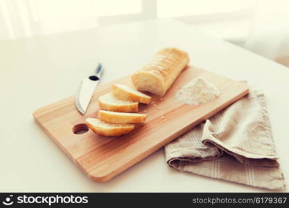 food, junk-food, diet and unhealthy eating concept - close up of white bread or baguette and kitchen knife on wooden cutting board