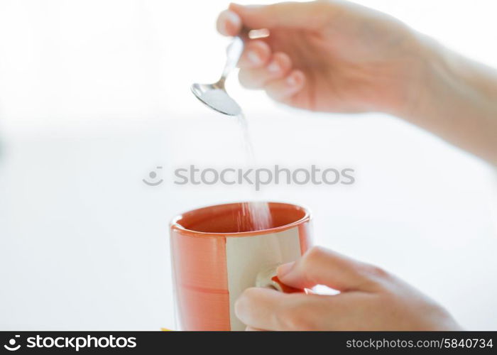 food, junk-food, drinks and unhealthy eating concept - close up of woman hands with spoon adding sugar to tea cup