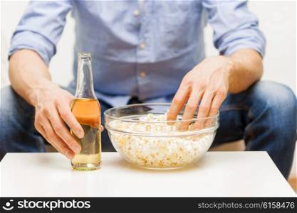 food, junk-food, unhealthy eating and people concept - close up of man with popcorn and beer bottle at home