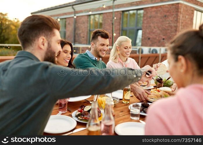 food, leisure and people concept - happy friends eating burgers at dinner party on rooftop in summer. friends eating burgers at dinner party on rooftop